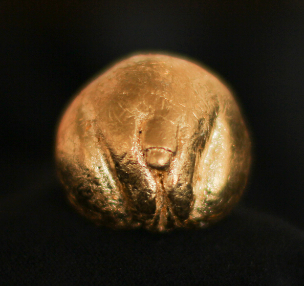 A photo of an orb, shining like metal gold. The start of thighs create the structure for labia and a t-cock. 